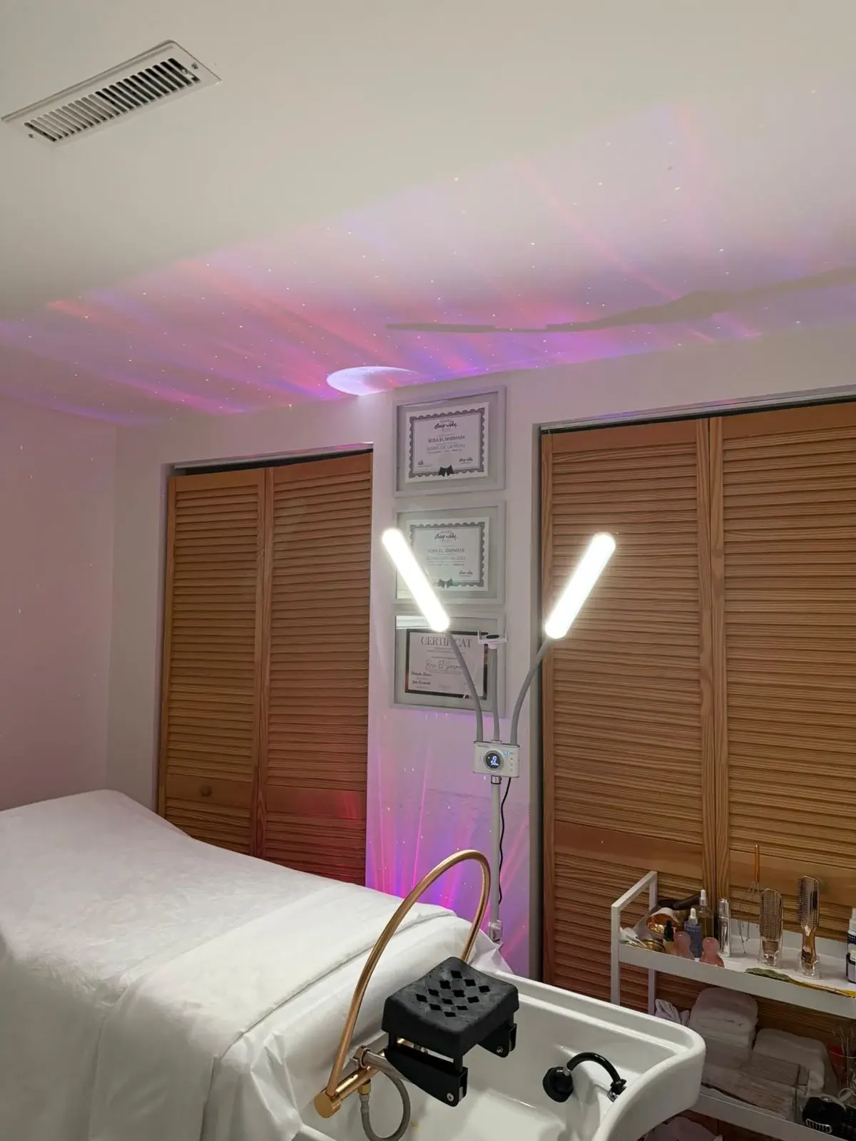 À l'intérieur du spa Soin Beauté Rosa à Laval : vasque de soins pour la tête, table de soins et luminaires apaisants en forme de galaxie au plafond.